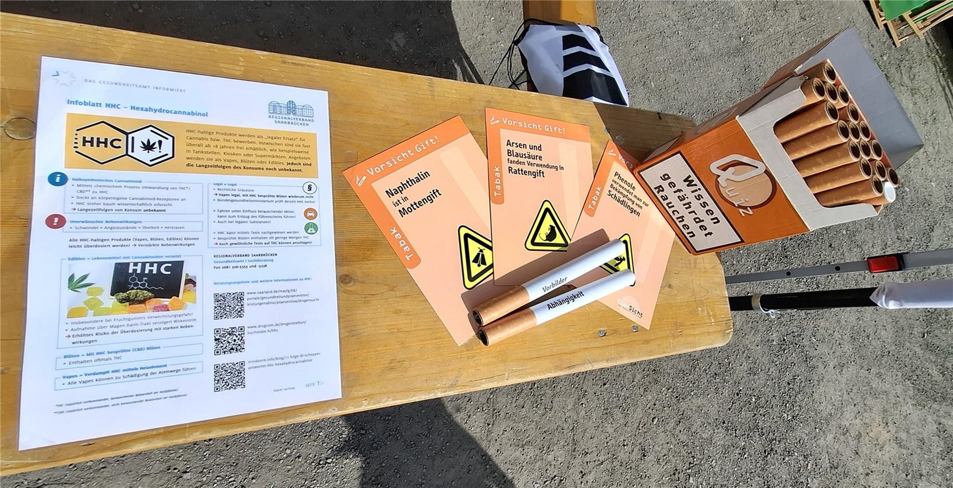 auf einem Biertisch liegen ein INfo-Plakat zu den Risiken von Zigaretten, außerdem überdimensional große, unechte Zigaretten.