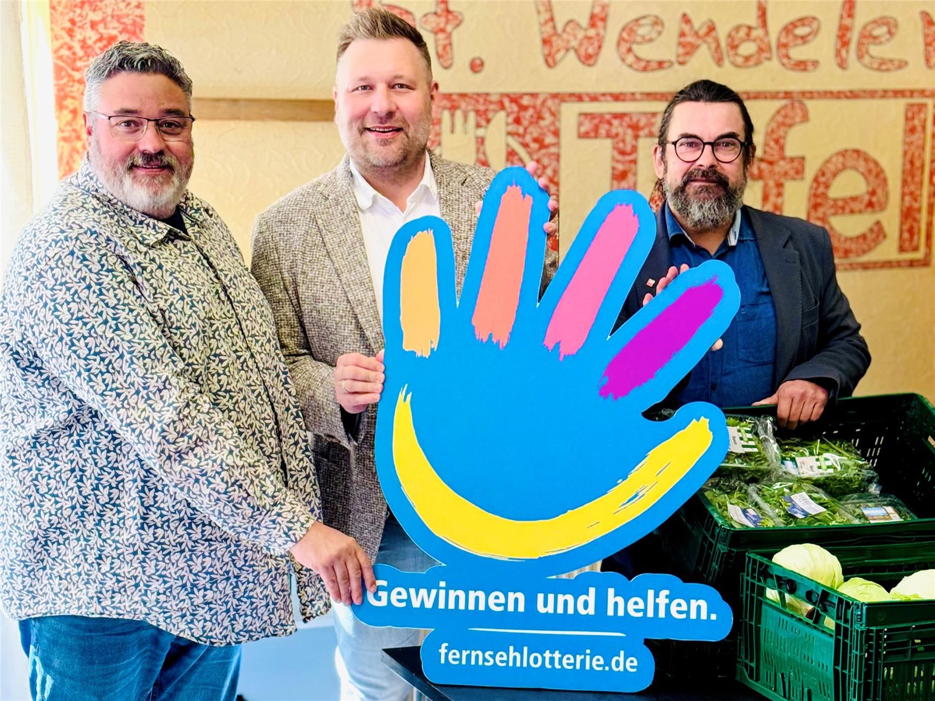 Hendrik Born und Thomas Mörsdorf vom Caritasverband halten gemeinsam mit Herrn Masch von der dt. Fernsehlotterie eine Hand als Zeichen für die dt. Fernsehlotterie